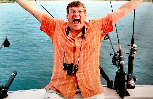 Robert G. Martin II seated on a fishing boat with his arms raised.